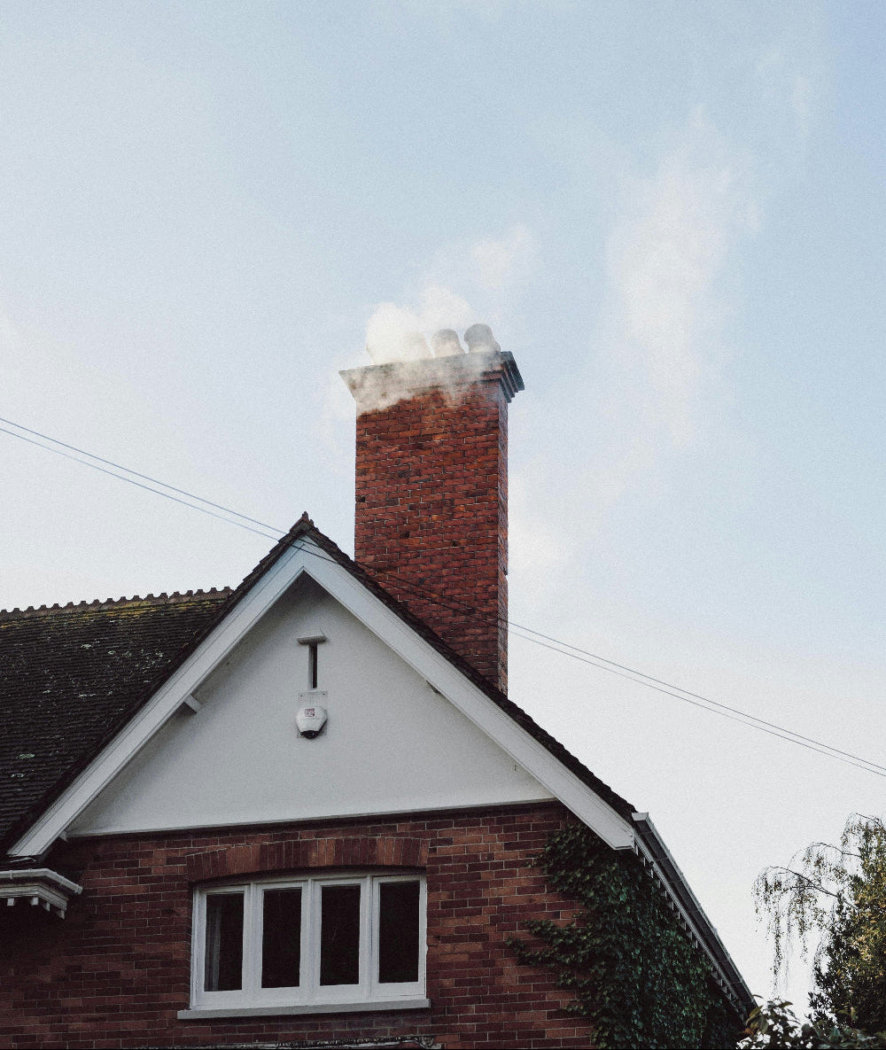 Brick chimney with smoke emitting from it against a clear blue sky.